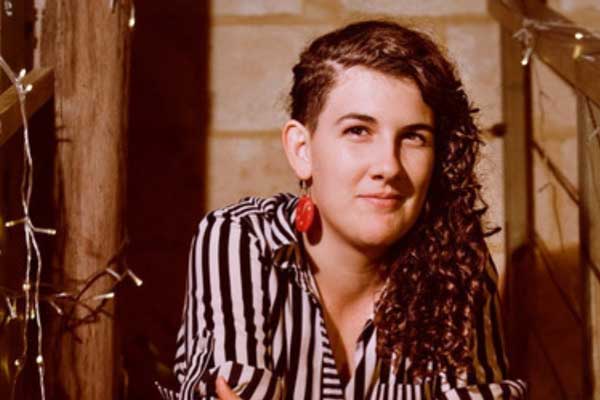 A portrait of Celilia Brandolini looking towards the camera, dressed in a a black and white striped shirt, hair combed to one side revealing an orange pebble-like earring.