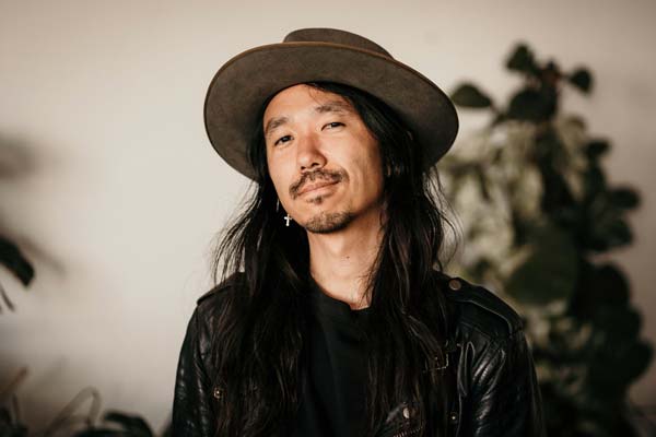 A Portrait of Johann Kim—founder of Pigeonhole, looking towards the camera. Johann is wearing a brown hat and a black leather jacket.